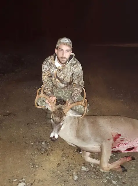 Hunter kneeling on the ground at night beside a harvested buck.