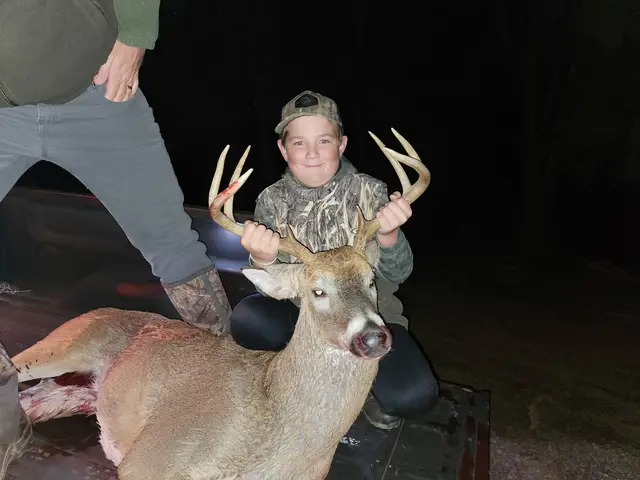 Young hunter holding a buck’s antlers in a pickup truck bed at night.