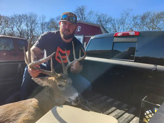 Hunter holding a buck’s antlers in a pickup truck bed on a sunny day.