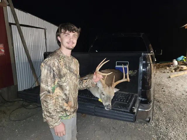 Young hunter in camouflage standing beside a buck on a pickup truck tailgate at night.