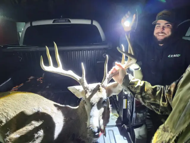 Two hunters beside a harvested buck and a pickup truck at night.