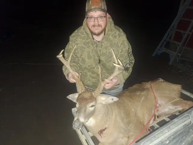 Hunter wearing a camouflage hood holding a buck’s antlers in a pickup truck bed at night.